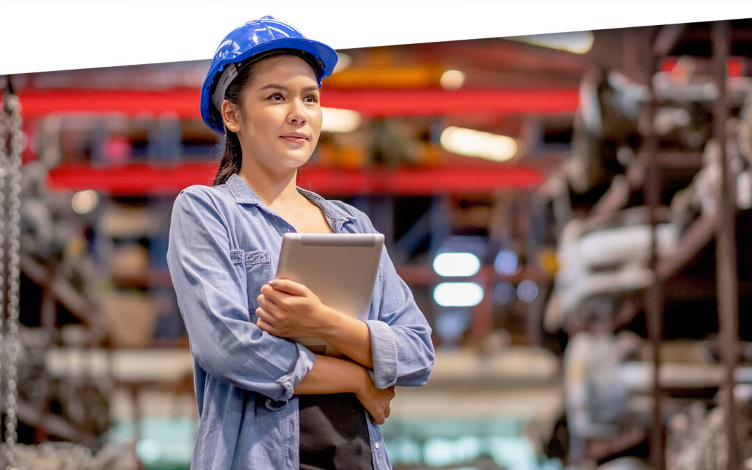 Retrato de una trabajadora de fábrica con casco azul sostiene una tableta y se para en el área de trabajo de repuestos. Concepto de confianza en trabajar con software de planificación de piezas de repuesto.